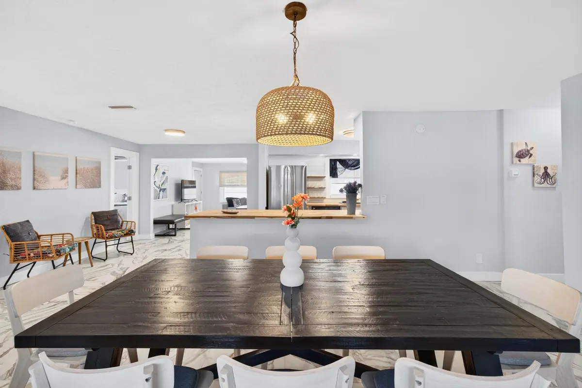 Dark timber dining table with a woven pendant above it, open to the kitchen beyond.