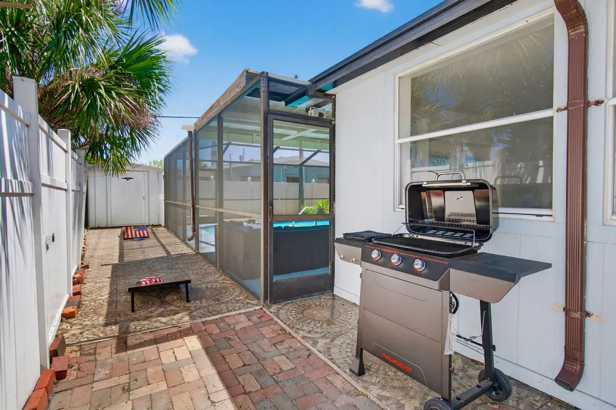 Gas grill on the brick paver side patio, beside the pool enclosure.
