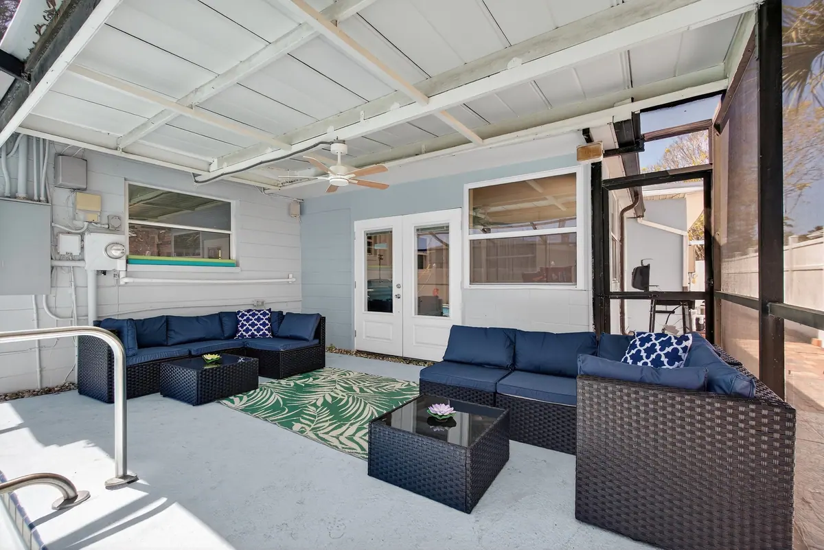 Covered lanai with navy outdoor sofas and a ceiling fan, opening onto the pool deck.