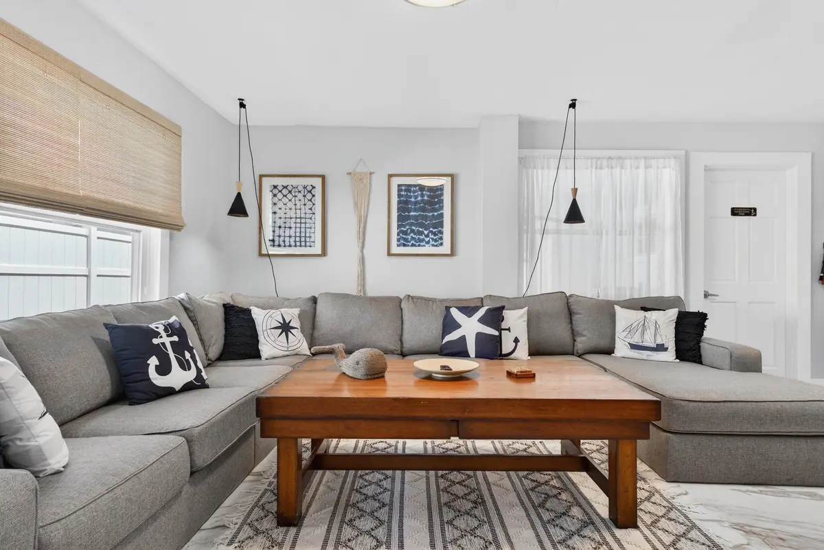 Living room with a large grey sectional, a timber coffee table and nautical prints on white walls.