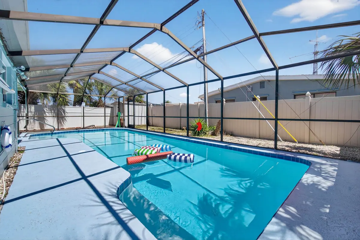 Private pool under a screened enclosure, its blue water bright against the pale deck and the palms outside.