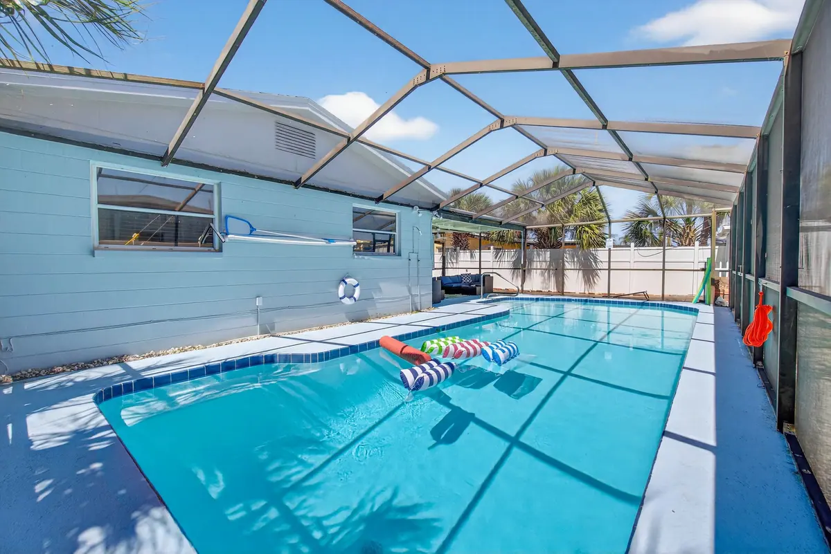 The full length of the screened pool, with the house running along one side and loungers at the far end.